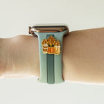 Smartwatch with a decorative band featuring pumpkins and leaves on a wrist against a neutral background