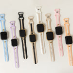 Six smartwatches with black rectangular screens are arranged in a row on a light off-white background, each featuring a different silicone strap color: light blue, lavender, black and white, white and black, cream and black, and peach and black.