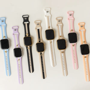 Six smartwatches with black rectangular screens are arranged in a row on a light off-white background, each featuring a different silicone strap color: light blue, lavender, black and white, white and black, cream and black, and peach and black.